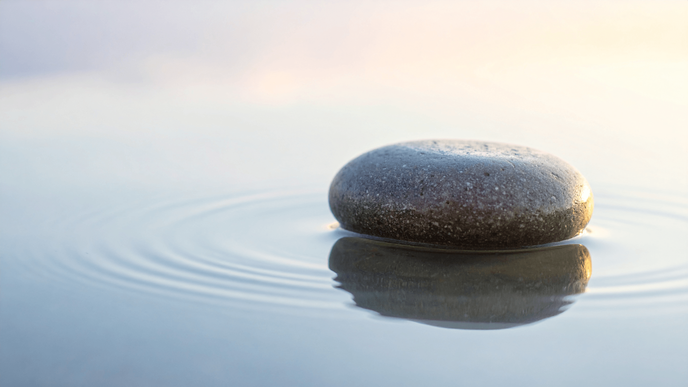 Stone resting in calm water with gentle ripples symbolising emotional boundaries and stopping people pleasing