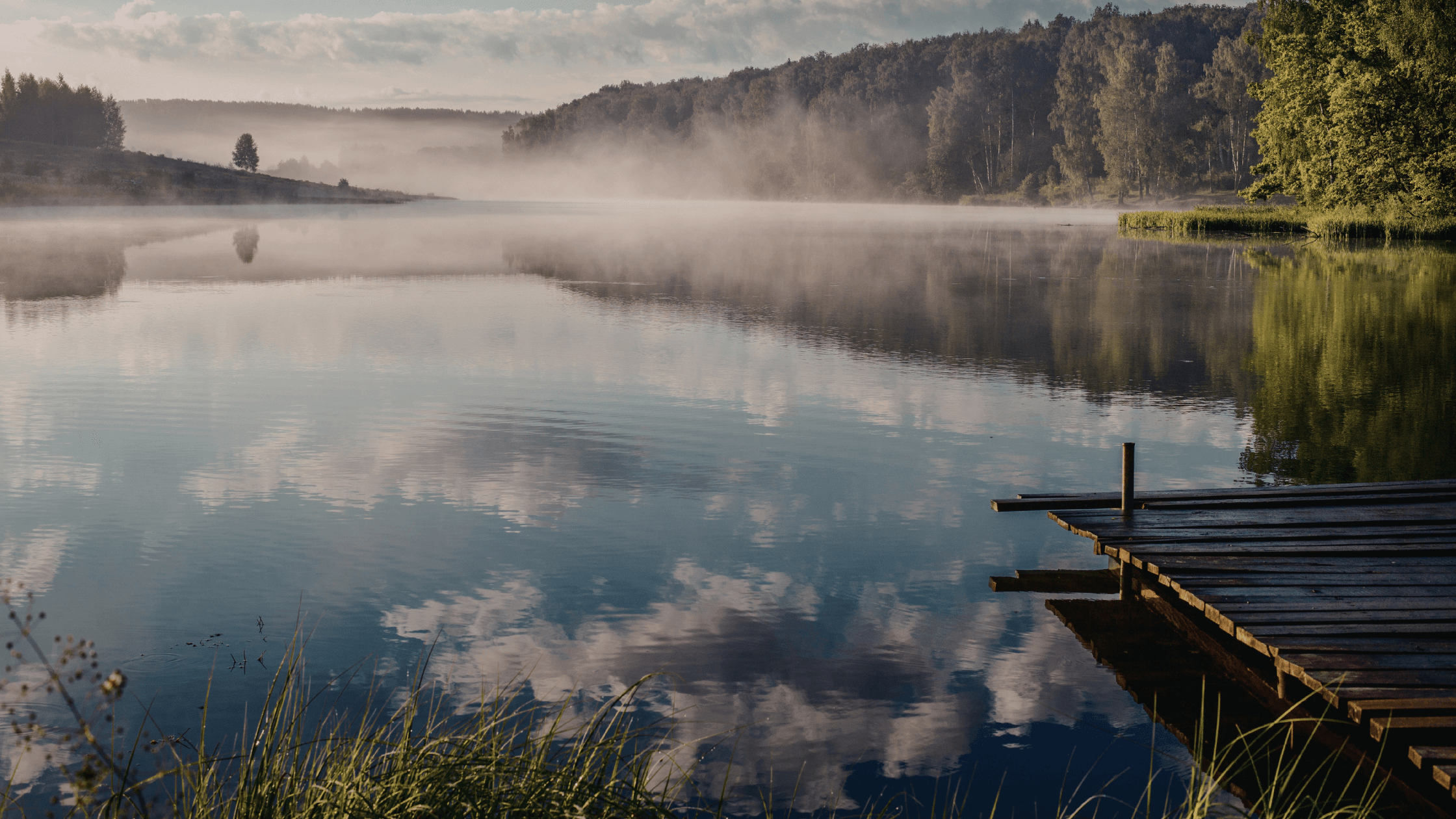 Mist rising over calm lake with wooden dock at sunrise, symbolising how to deal with overwhelm and return to emotional steadiness.